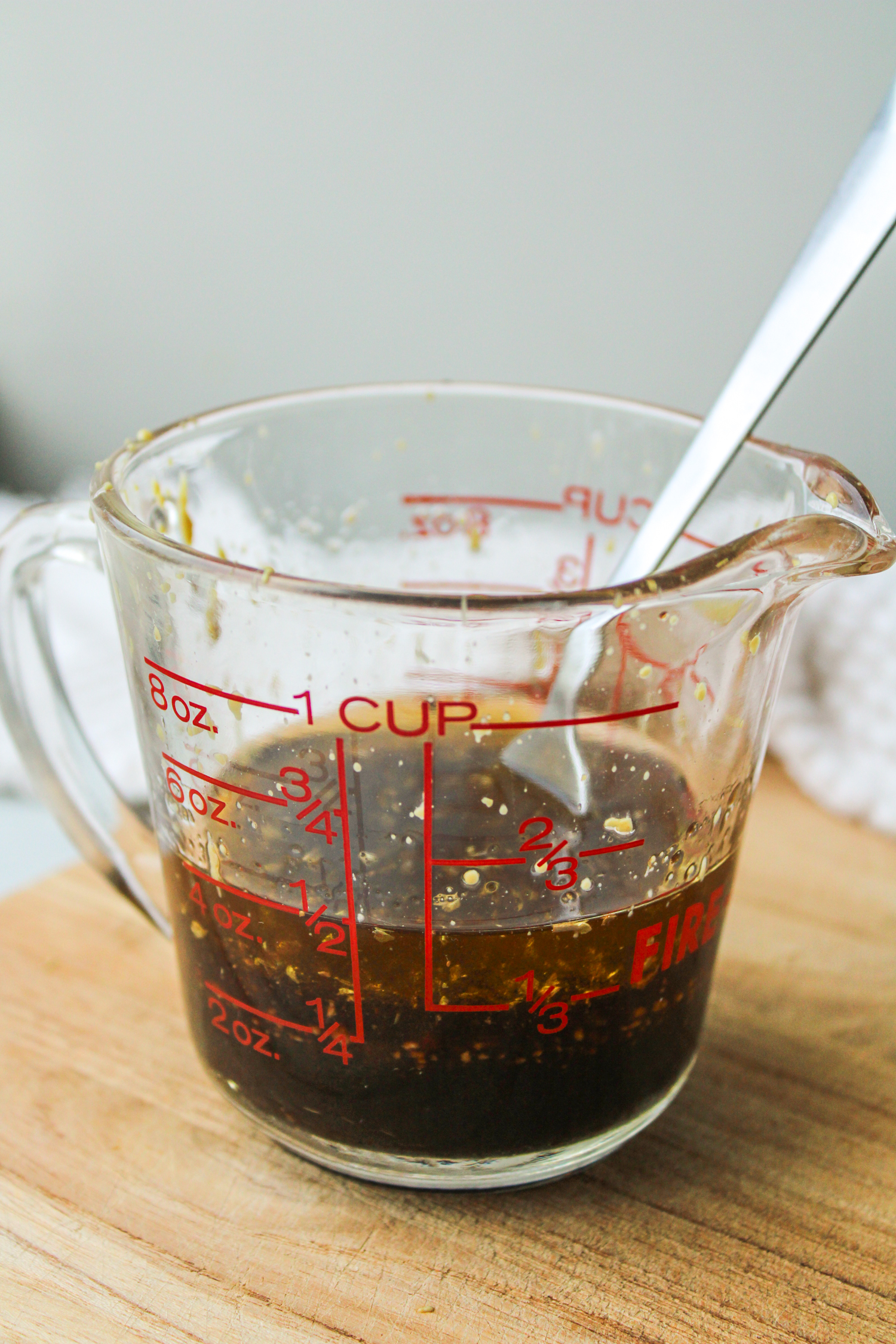 maple balsamic dressing in a glass measuring cup on a wooden cutting board