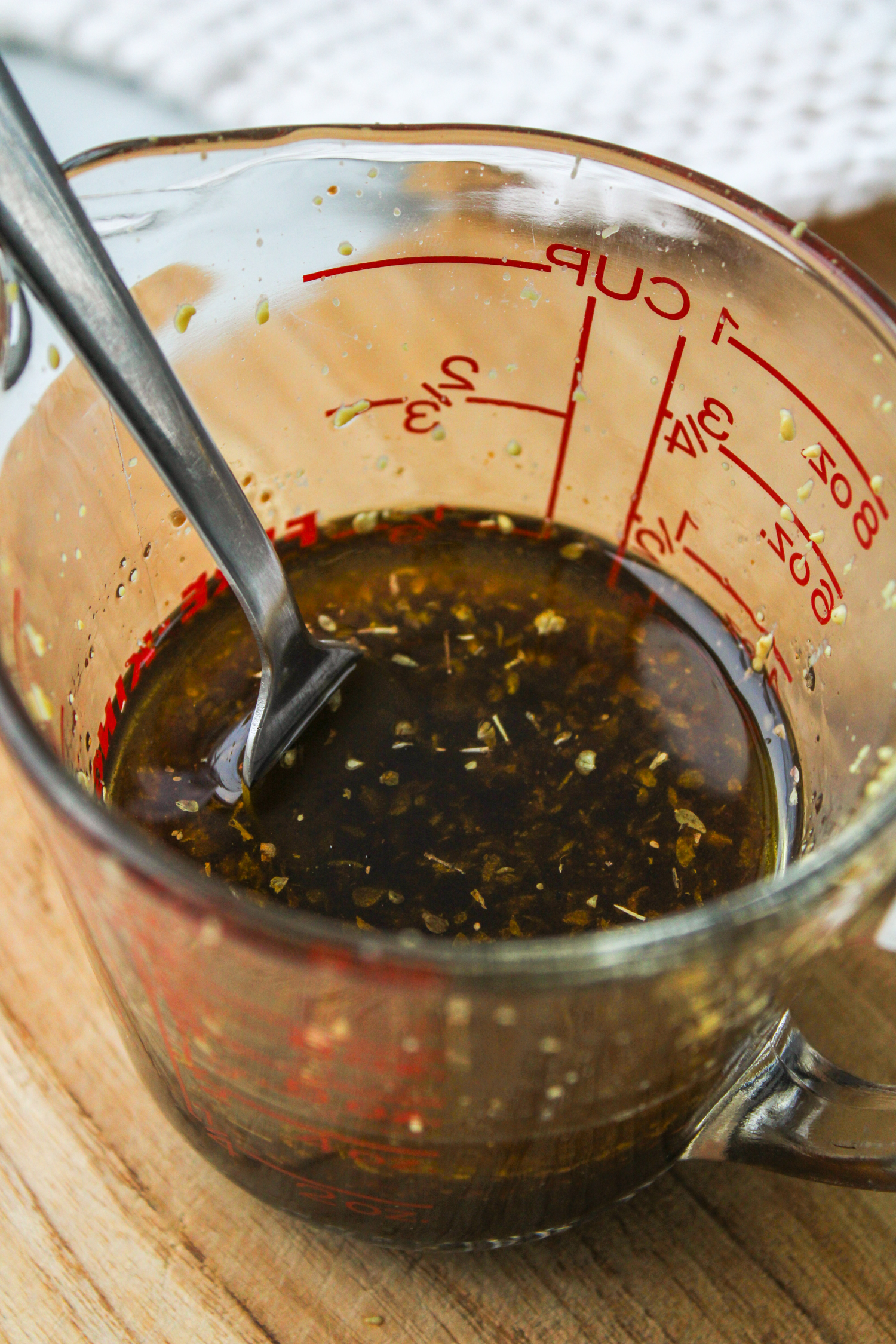 overhead shot of maple balsamic dressing in a glass measuring cup on a wooden cutting board