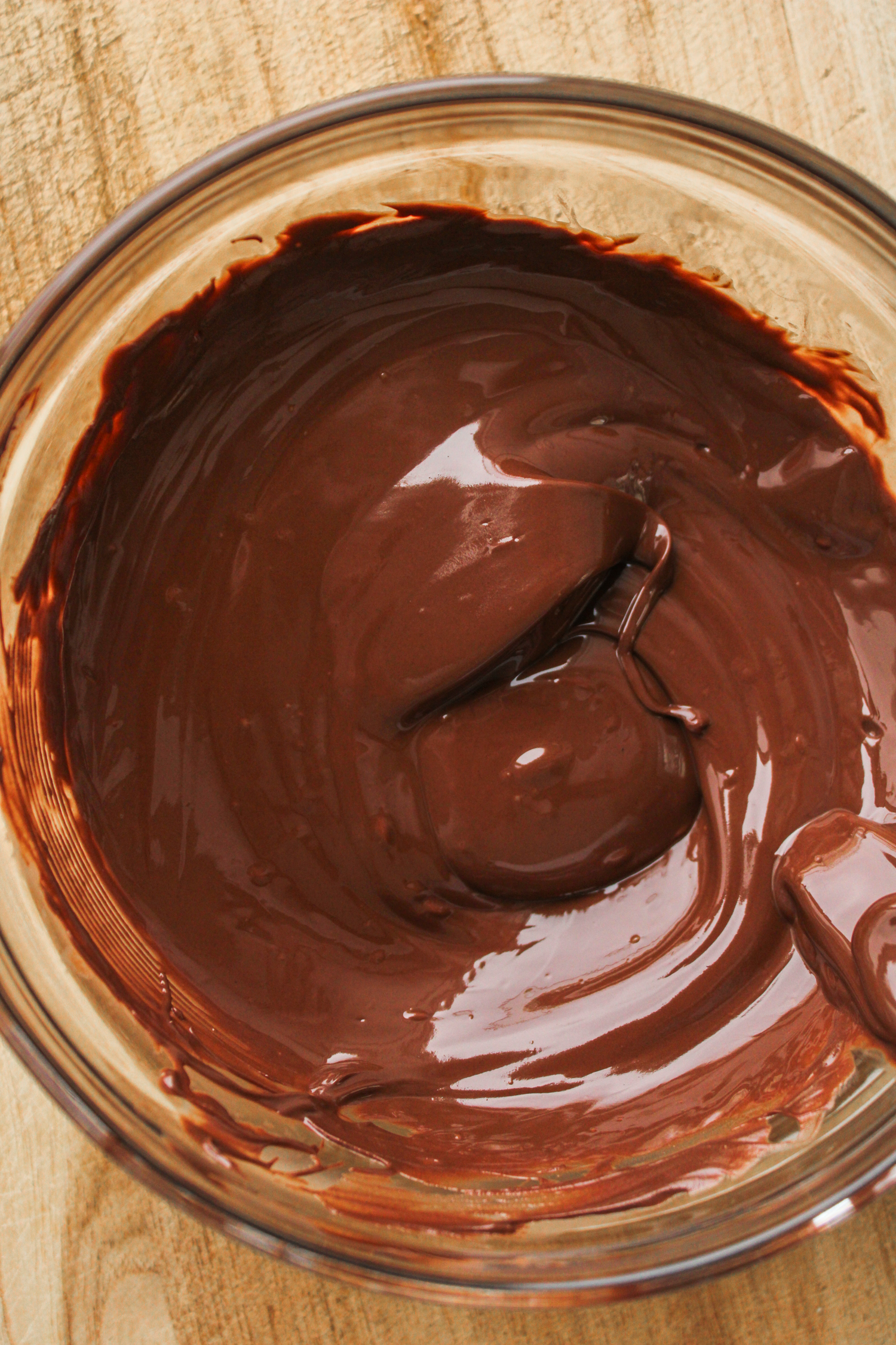 melted chocolate in a glass bowl on top of a wooden cutting board