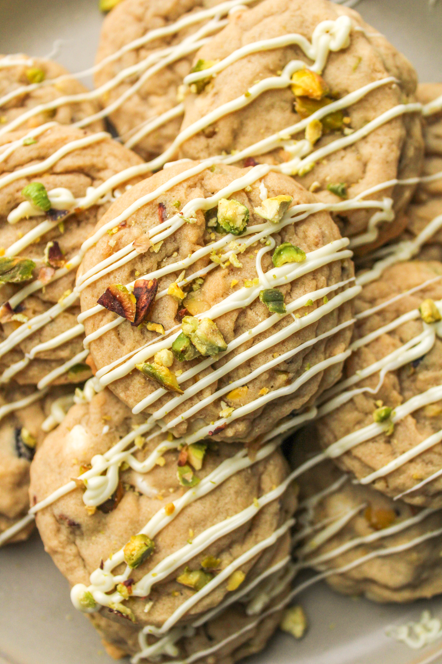 pistachio chocolate chip cookies layered on top of each other, drizzled in white chocolate and crumbled pistachios on top