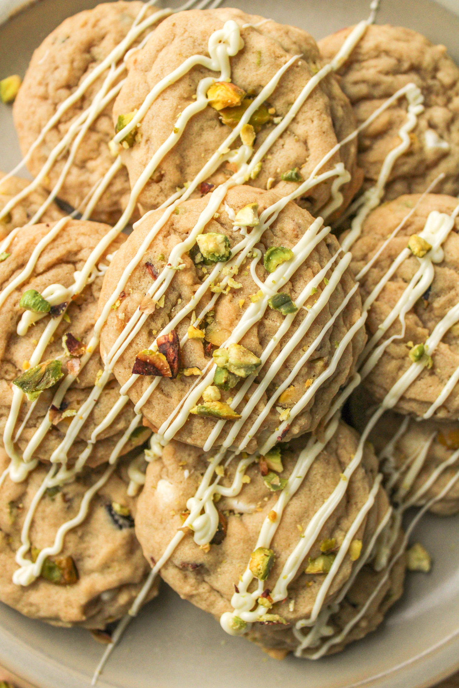 pistachio white chocolate chip cookies layered on top of each other, drizzled in white chocolate and crumbled pistachios on top