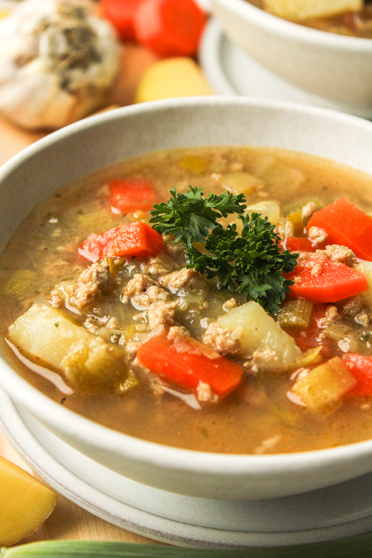 close up profile shot of potato leek soup with chicken topped with fresh parsley in a white ceramic bowl