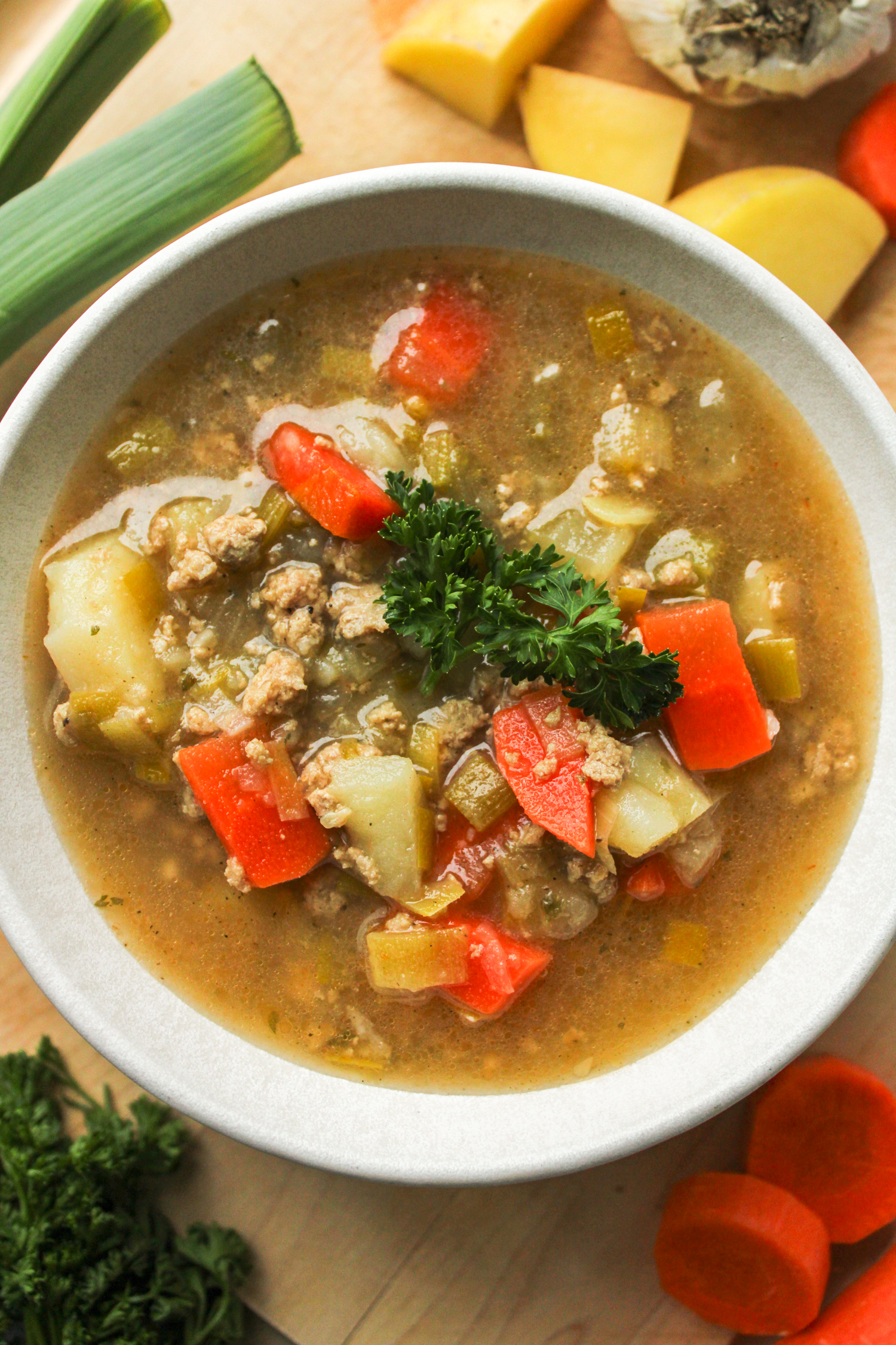 overhead shot of potato leek soup with chicken topped with fresh parsley in a white ceramic bowl with fresh ingredients surrounding it