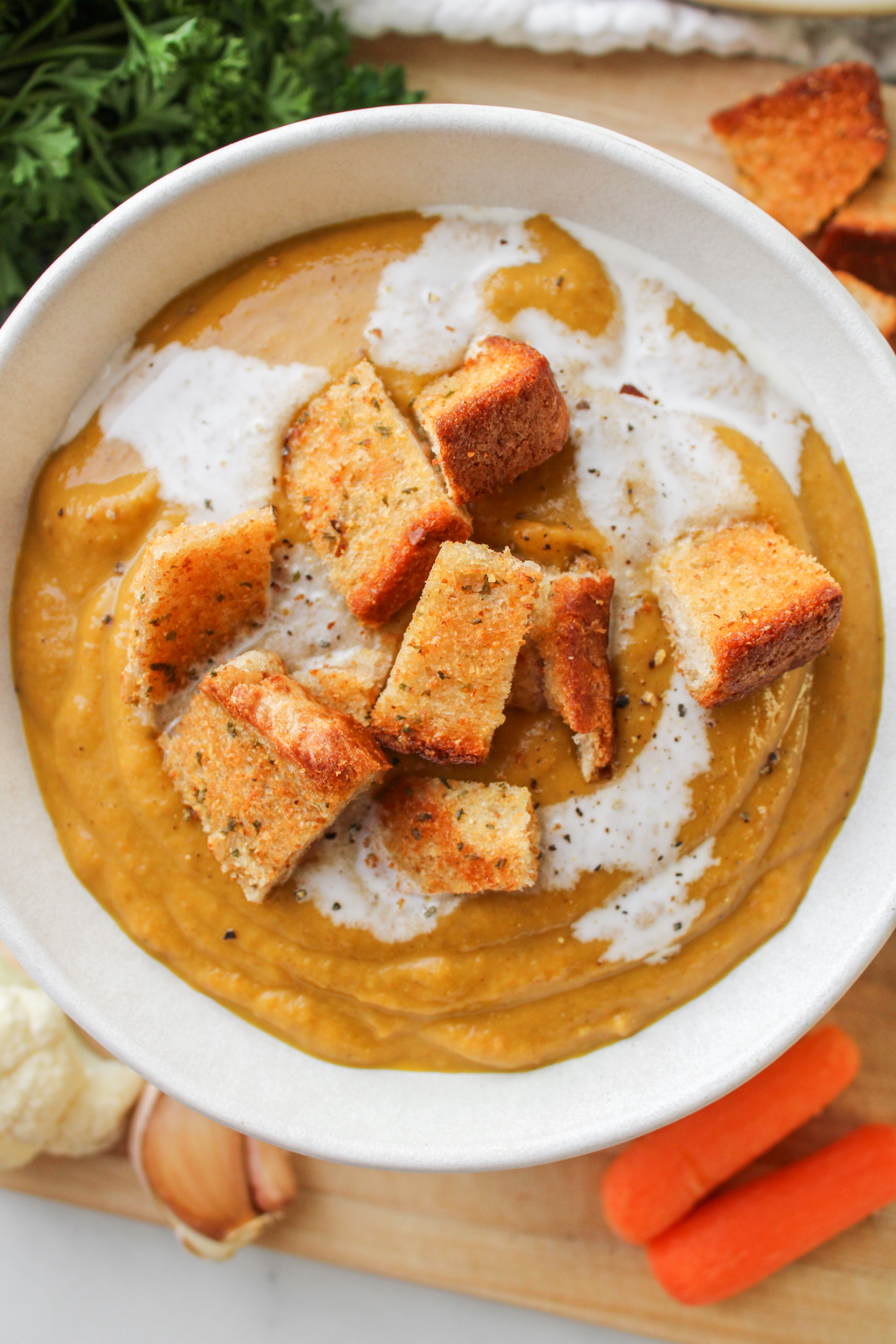 carrot and lentil soup with garlic bread bites in a white ceramic bowl on a wooden board