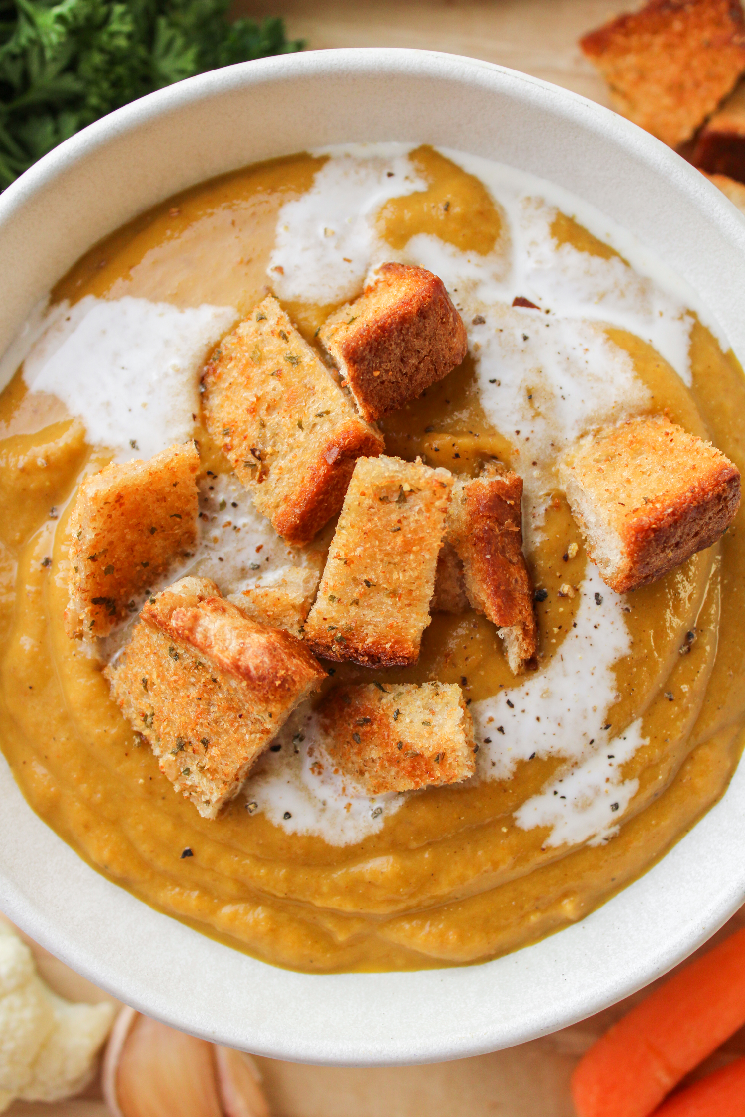 close up of carrot and lentil soup with garlic bread bites in a white ceramic bowl on a wooden board