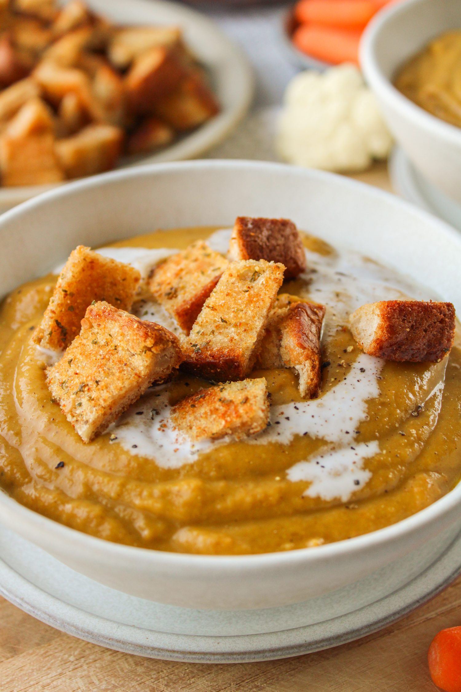 profile shot of carrot and lentil soup with garlic bread bites in a white ceramic bowl on a wooden board