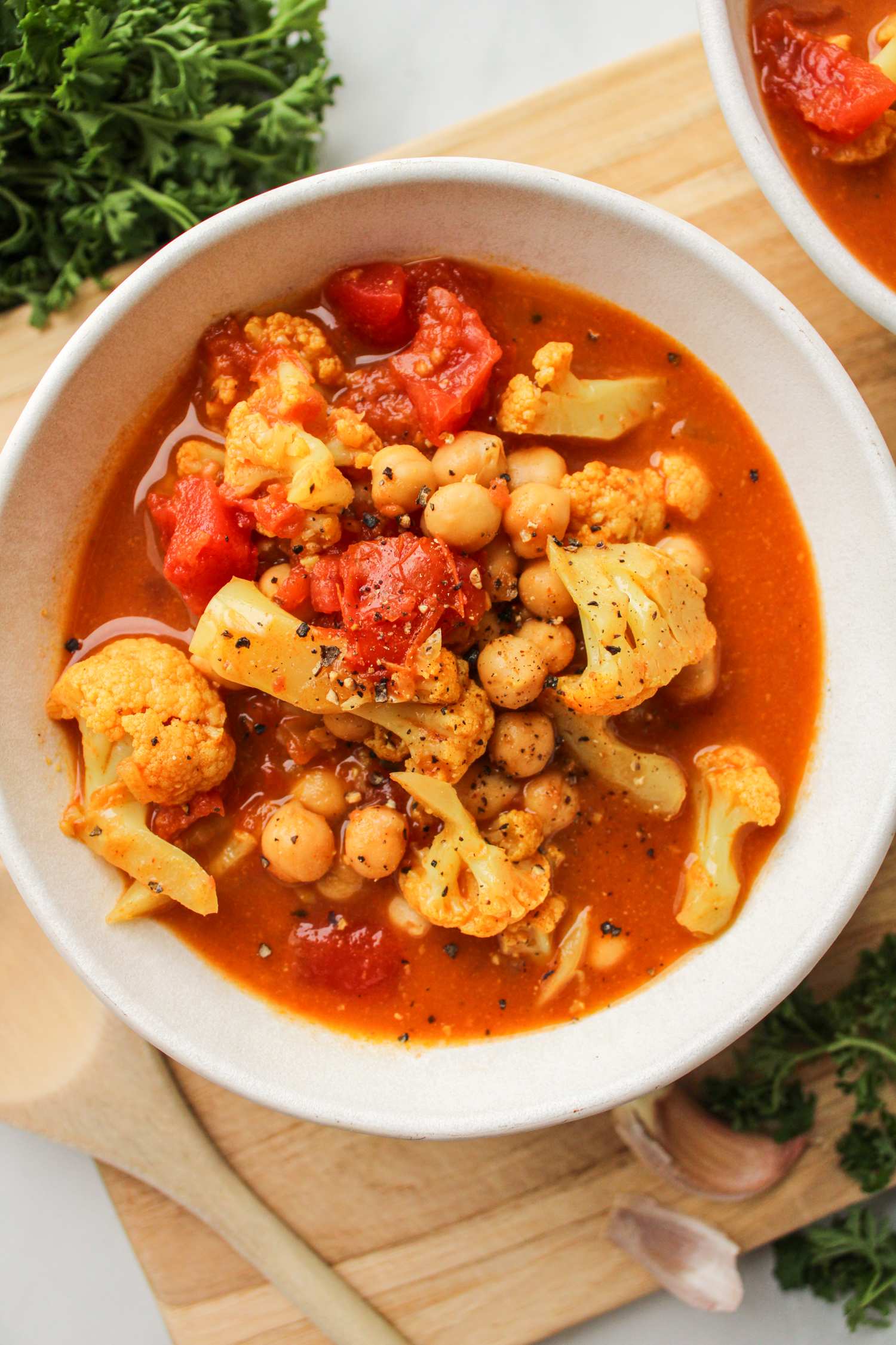 cauliflower chickpea curry in a white ceramic bowl on top of a wooden cutting board