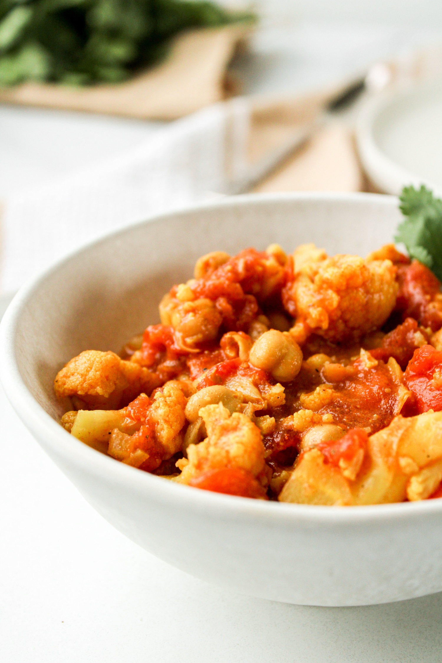 close up profile shot of chickpea curry in a white ceramic bowl on top of a white ceramic plate