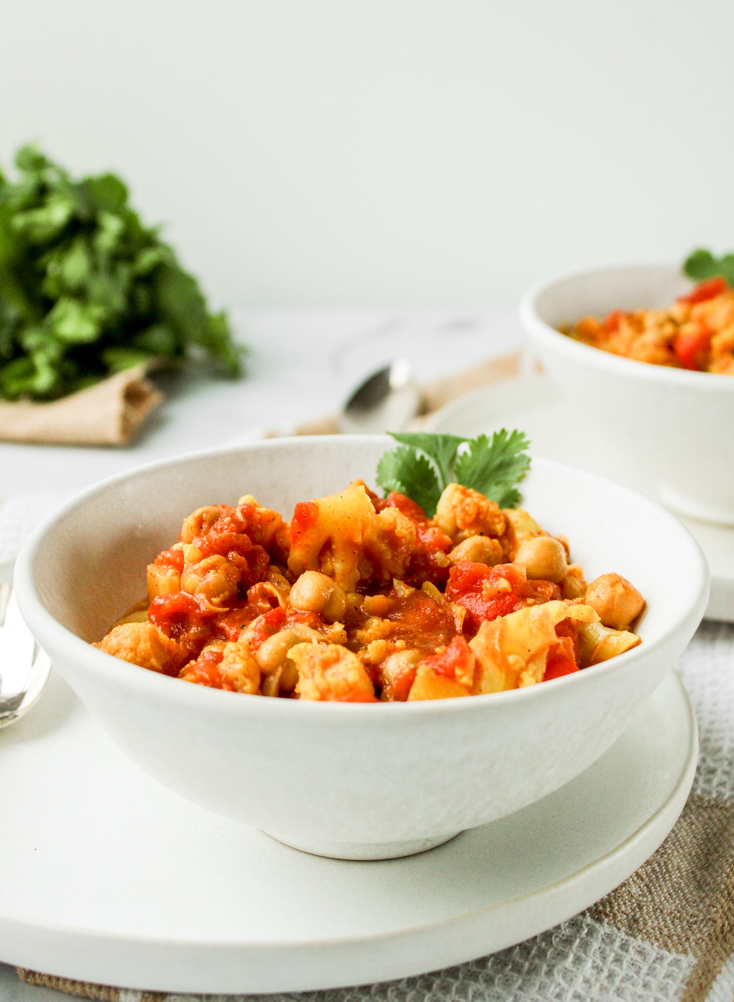 profile shot of cauliflower curry in a white ceramic bowl on top of a white ceramic plate