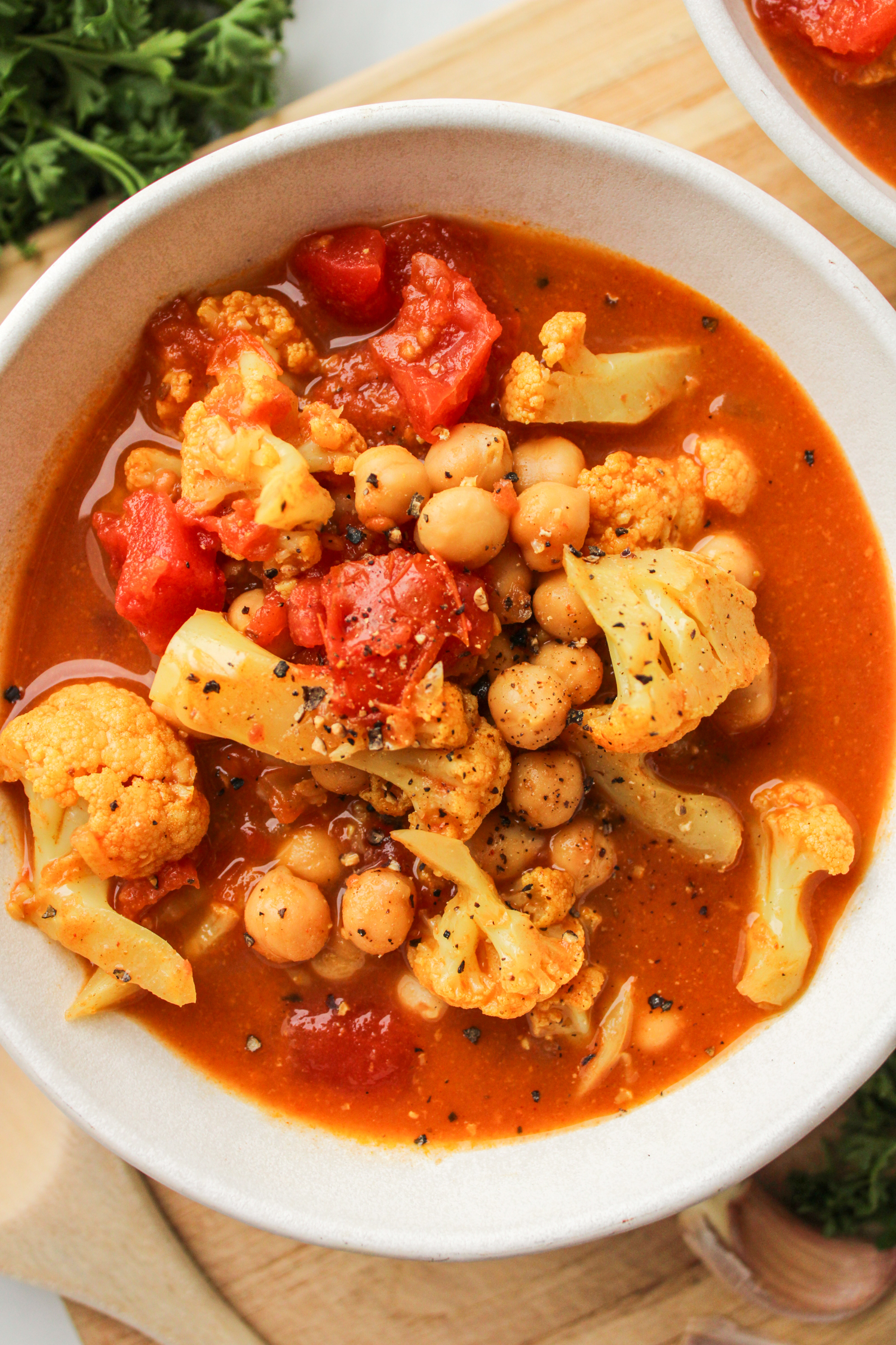 chickpea cauliflower curry in a white ceramic bowl on top of a wooden cutting board