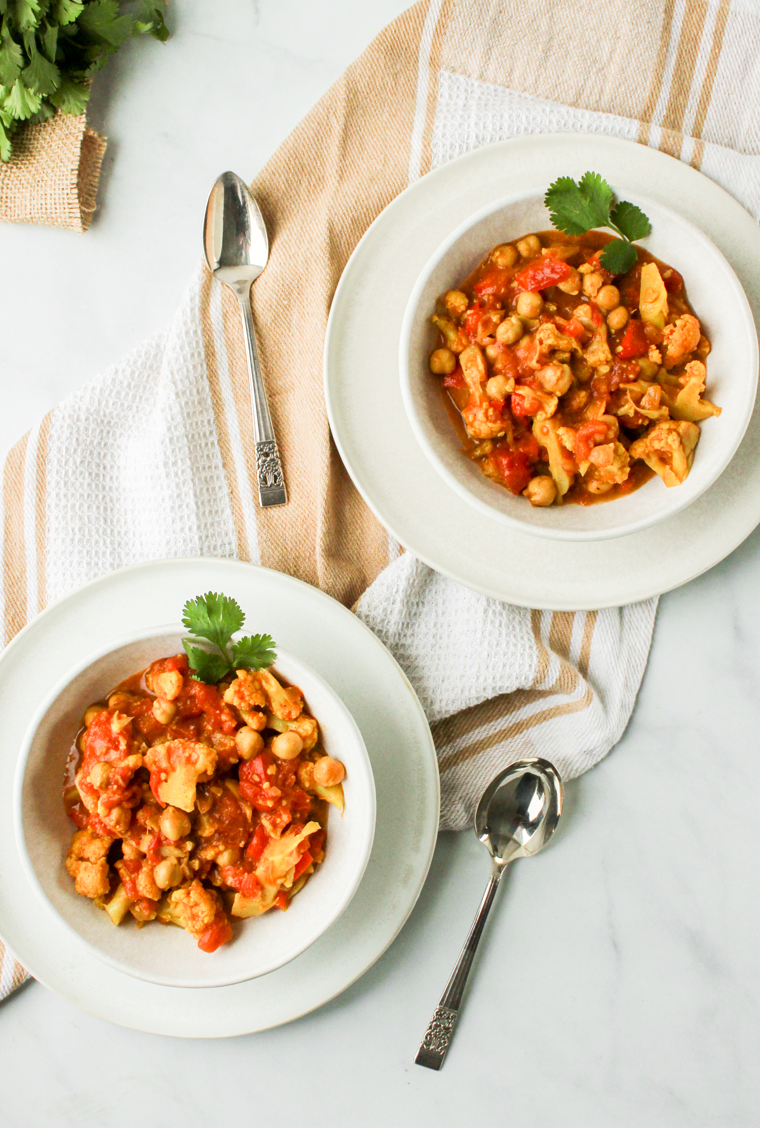 overhead shot of two bowls of chickpea curry each in a white ceramic bowl on top of a white ceramic plate