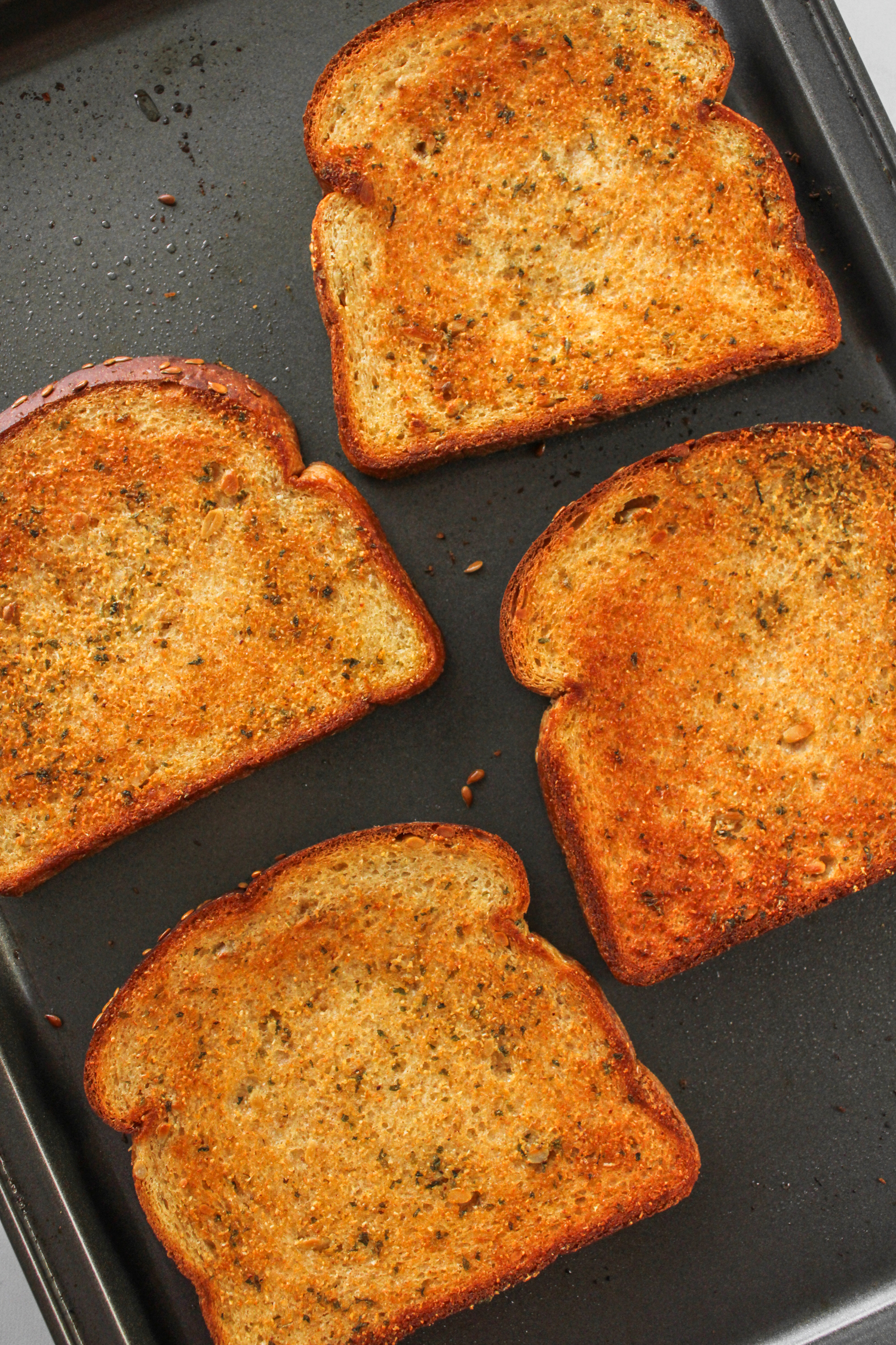 four slices of baking garlic bread spread out on a baking sheet