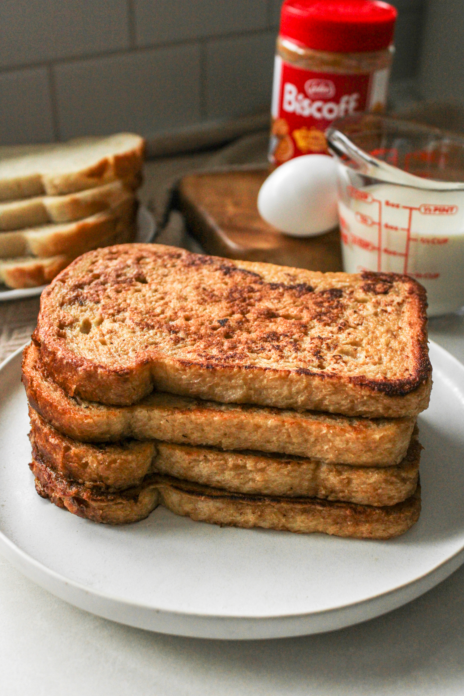 four slices of sourdough french toast stacked on top of a ceramic plate with ingredients in the back