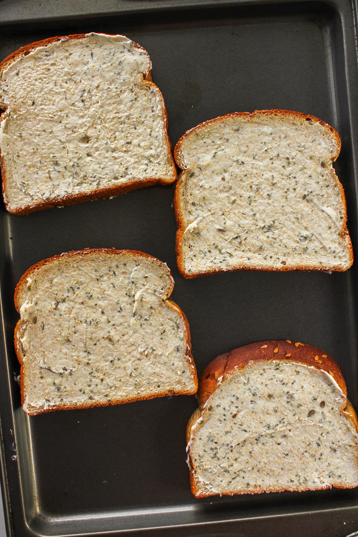 four slices of fresh bread topped with homemade garlic butter spread out on a baking sheet