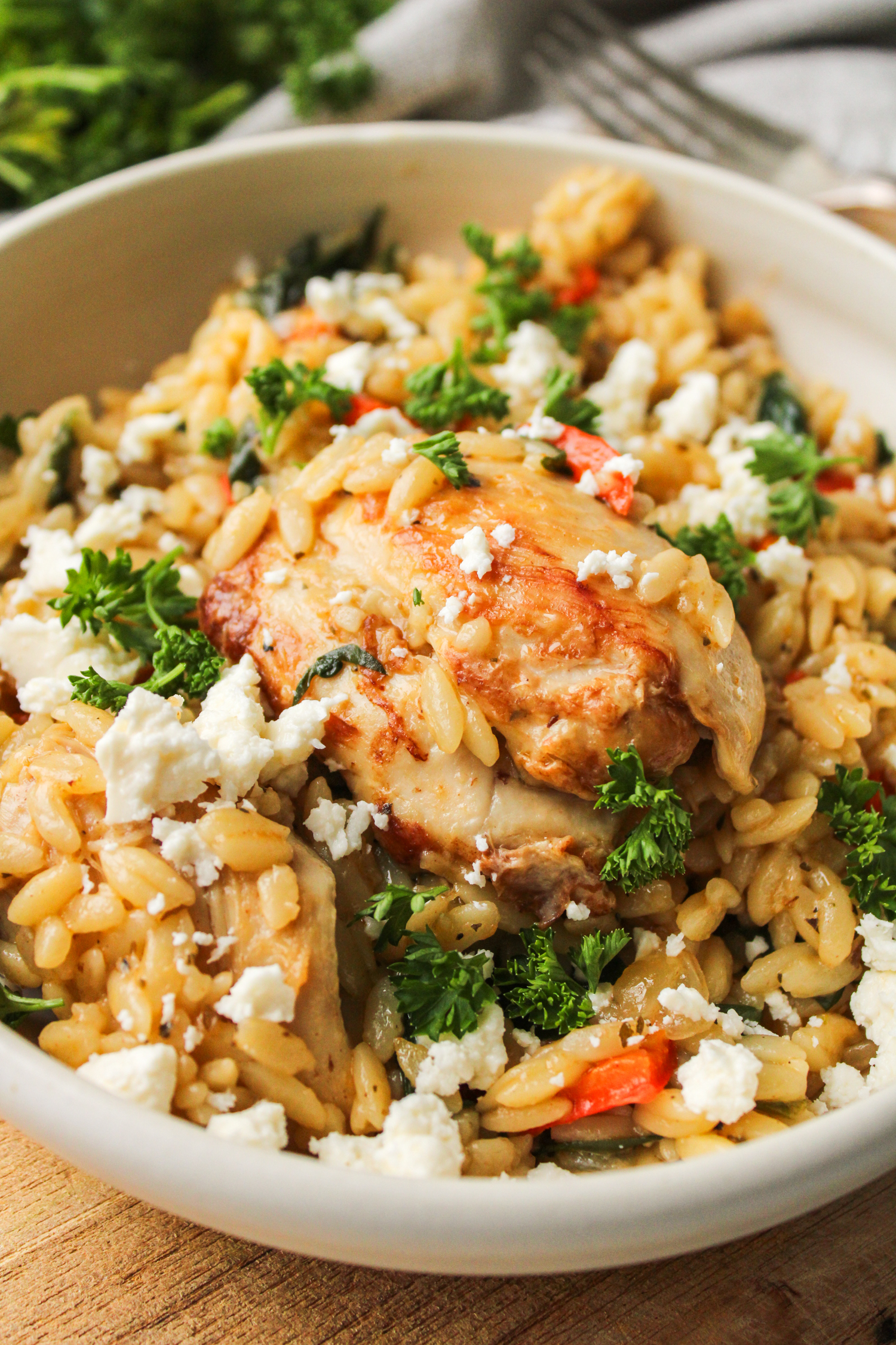 Mediterranean chicken orzo bake in a beige ceramic dish with feta and parsley on top