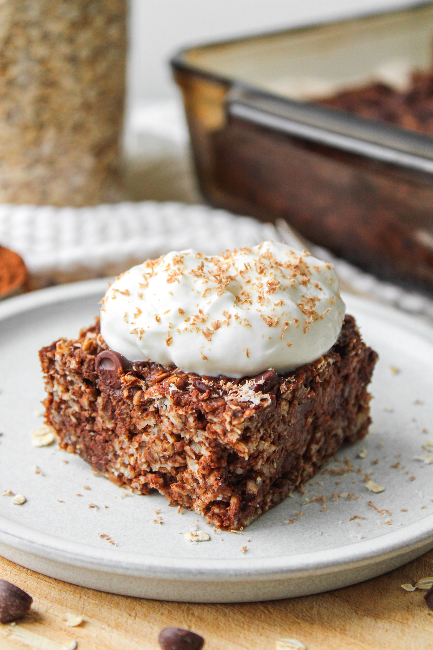 A square of double chocolate baked oatmeal topped with a dollop of Greek yogurt and chocolate shavings on top of a white ceramic plate