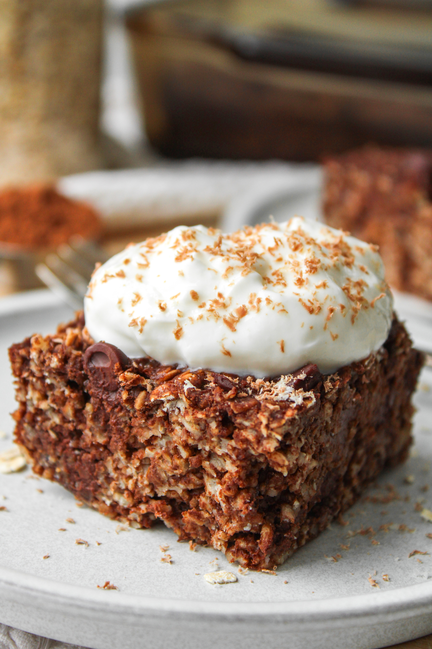 A close up of a square of double chocolate baked oatmeal topped with a dollop of Greek yogurt and chocolate shavings on top of a white ceramic plate