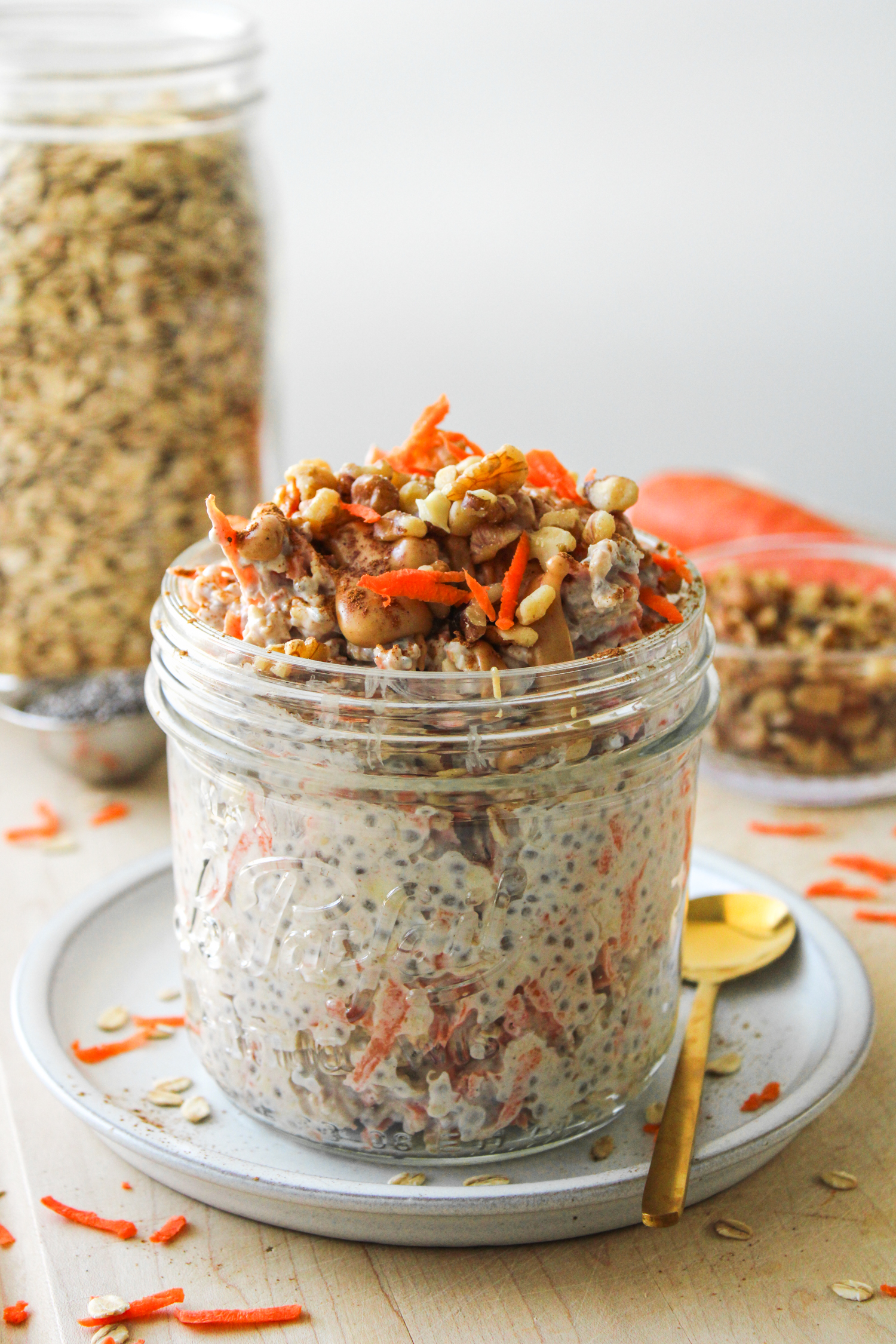 carrot overnight oats in a large glass mason jar on top of a grey ceramic plate on a wooden cutting board