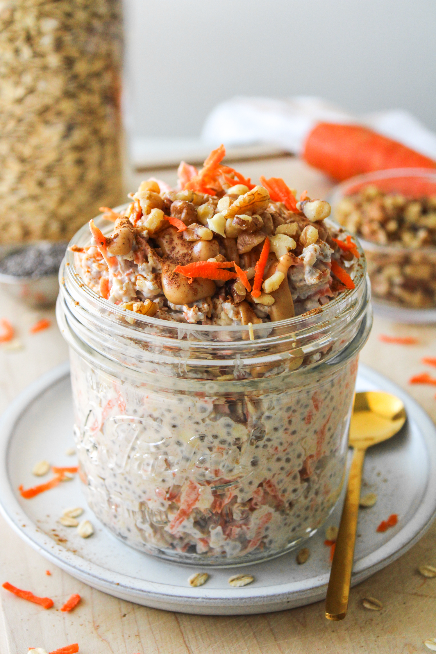 carrot cake overnight oats in a large glass mason jar topped with grated carrot, walnuts, cinnamon and peanut butter