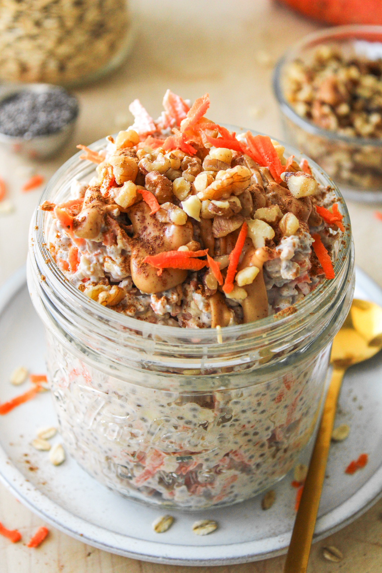 a closer up angled shot of carrot cake overnight oats in a large glass mason jar topped with grated carrot, walnuts, cinnamon and peanut butter