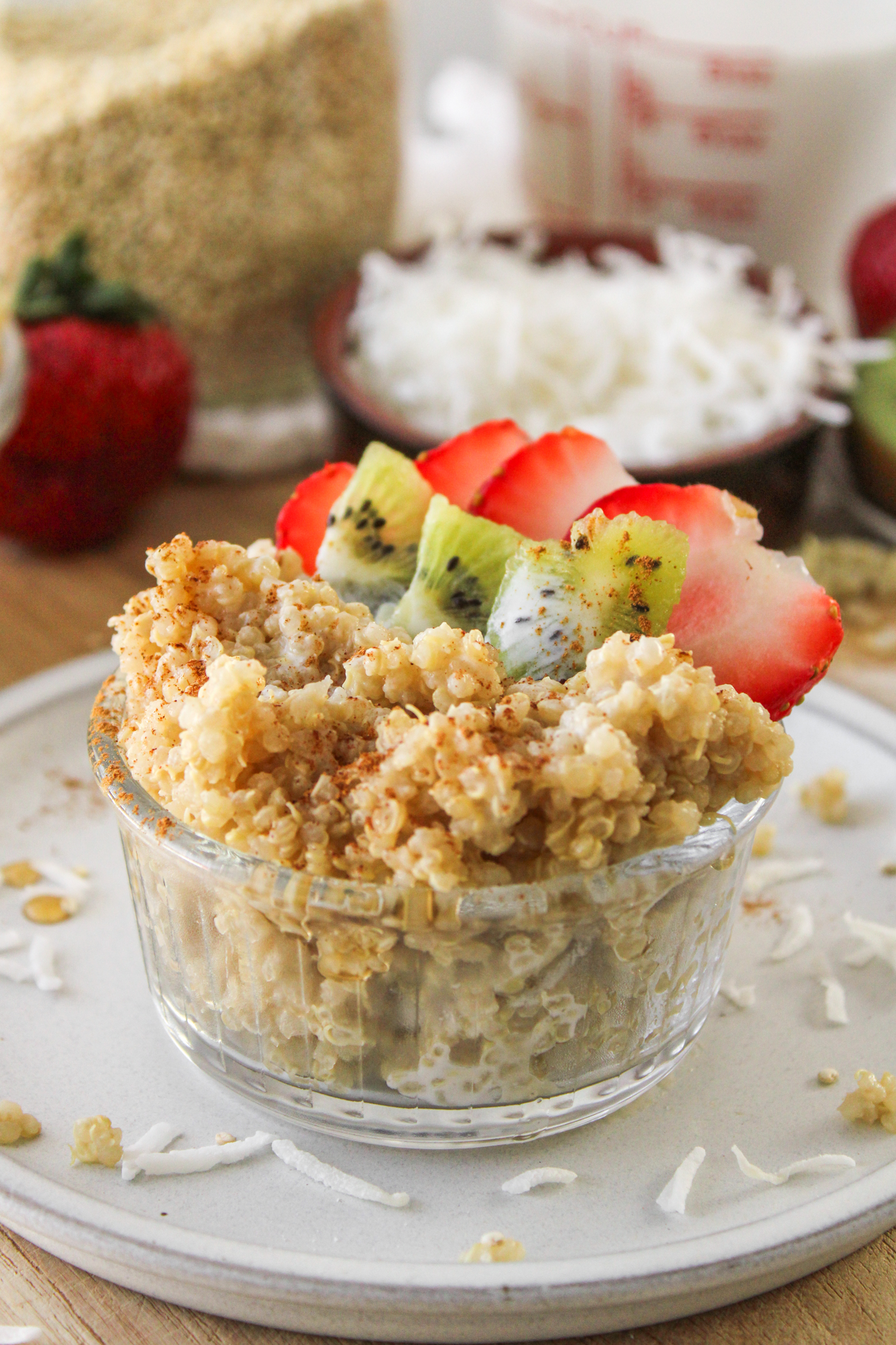 close up shot of quinoa coconut milk porridge in a small glass bowl topped with kiwi and strawberries