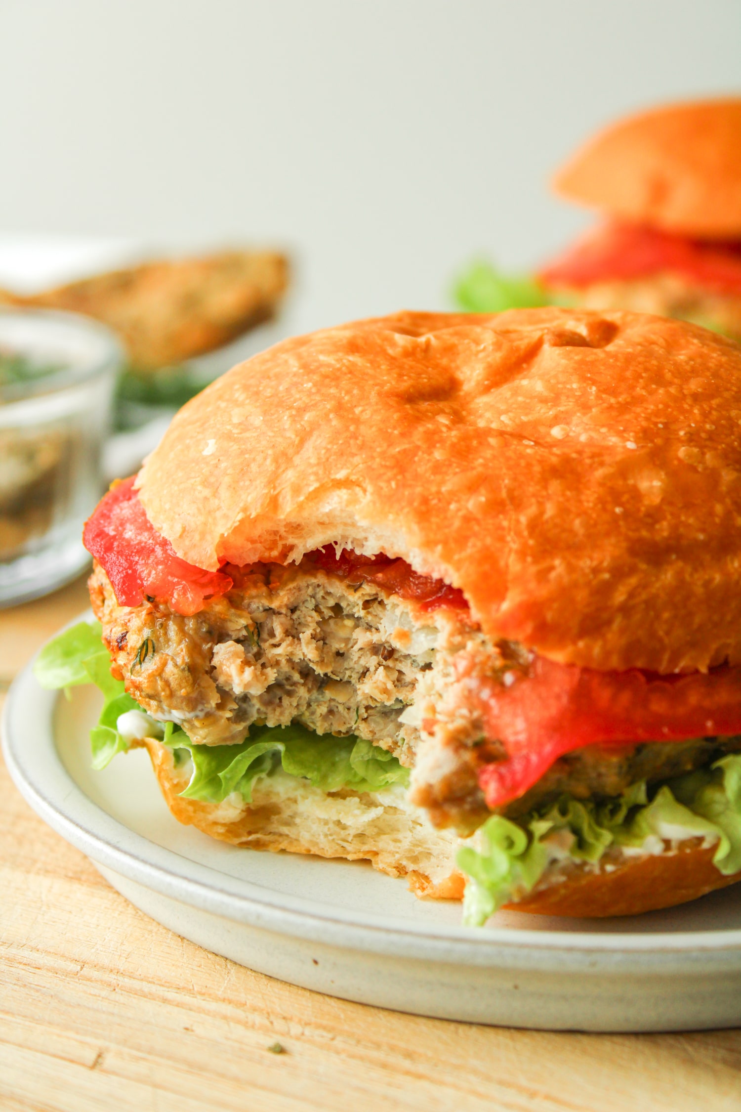 close up bite shot of air fryer turkey burger with lettuce, tomato and tzatziki in a hamburger bun on a grey ceramic plate