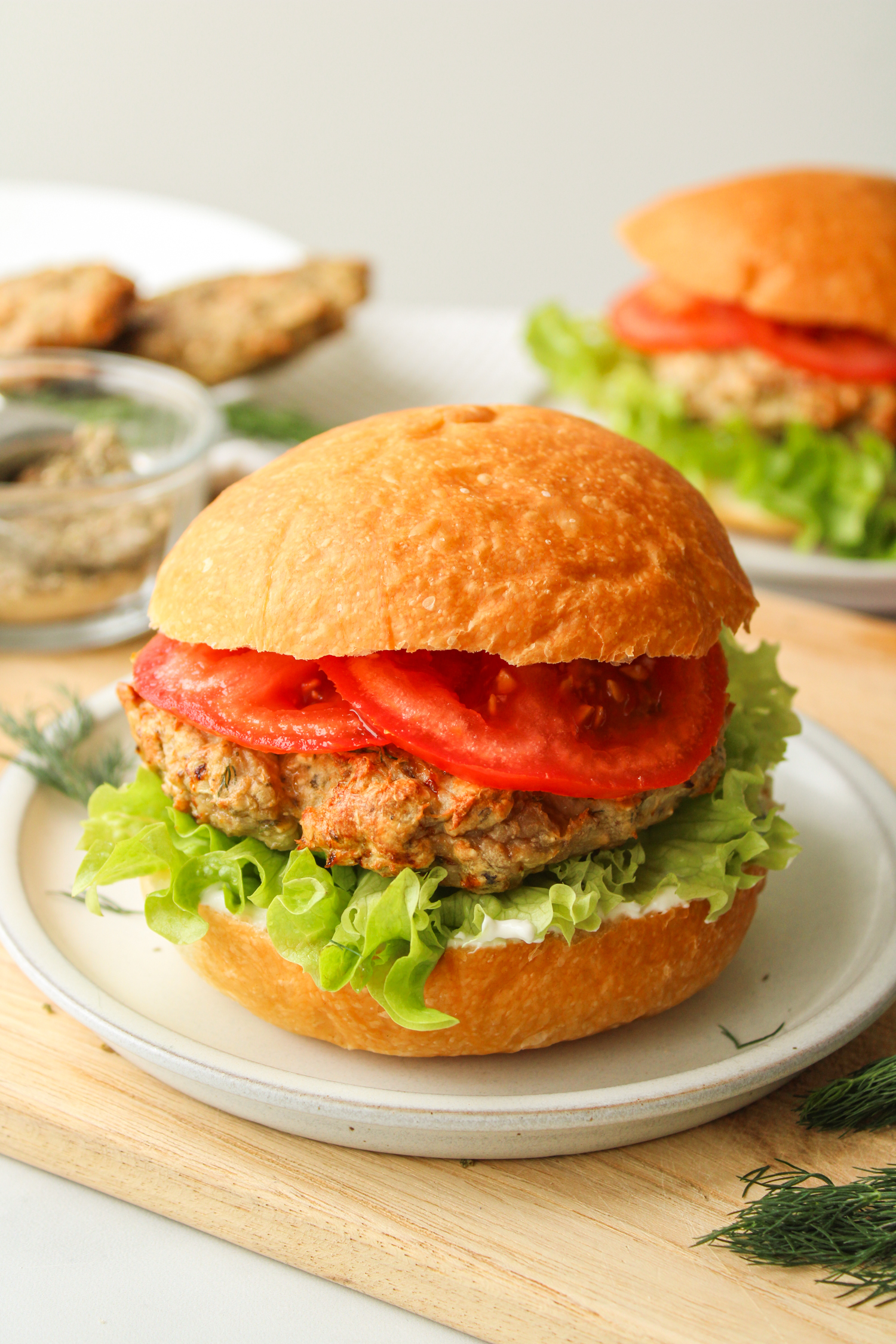 air fryer turkey burger with lettuce, tomato and tzatziki in a hamburger bun on a grey ceramic plate on top of a wooden cutting board