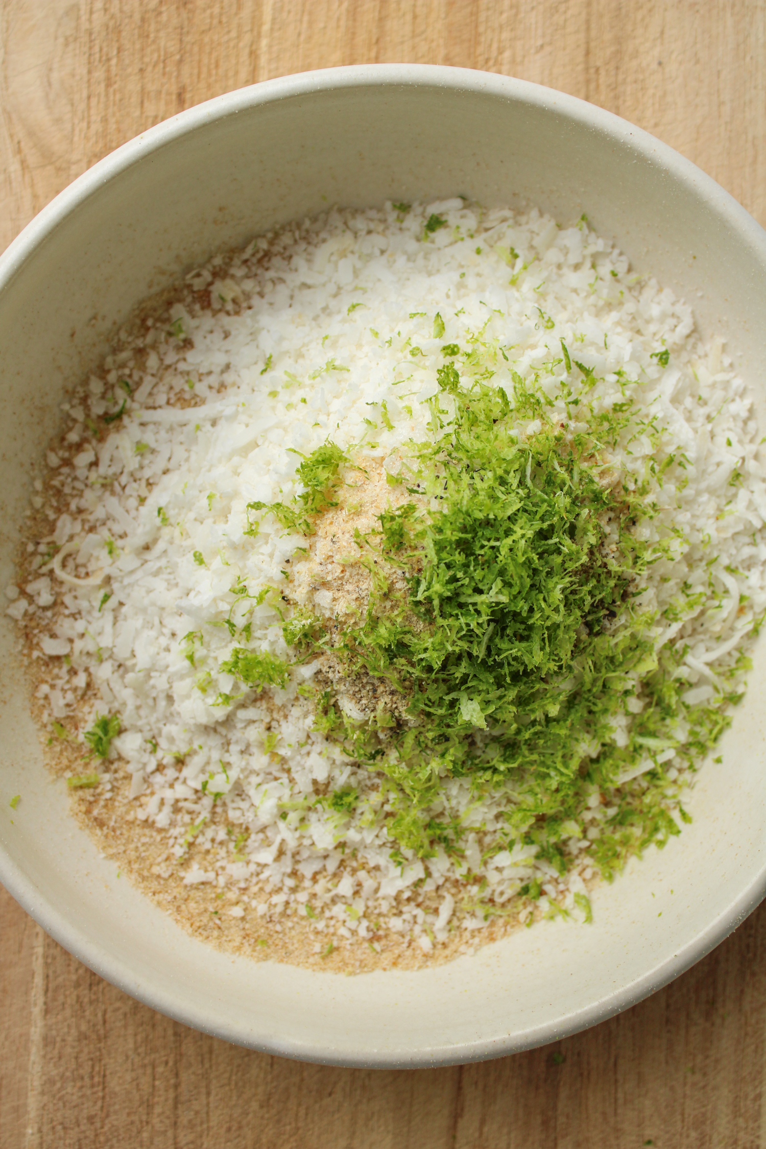 ingredients for the coconut panko crumb mixture in a white ceramic bowl on a wooden cutting board