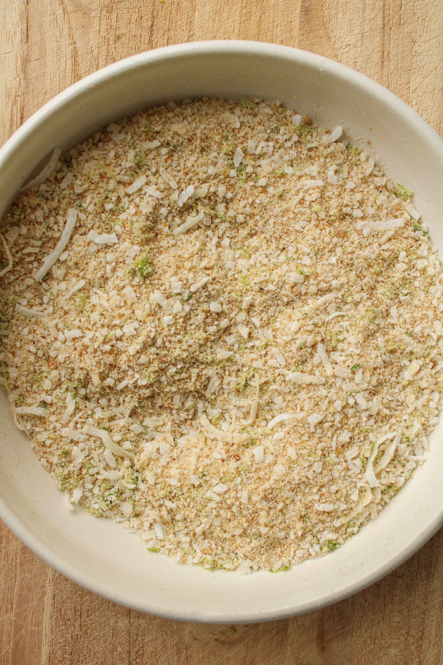 coconut panko crumb mixture in a white ceramic bowl on a wooden cutting board