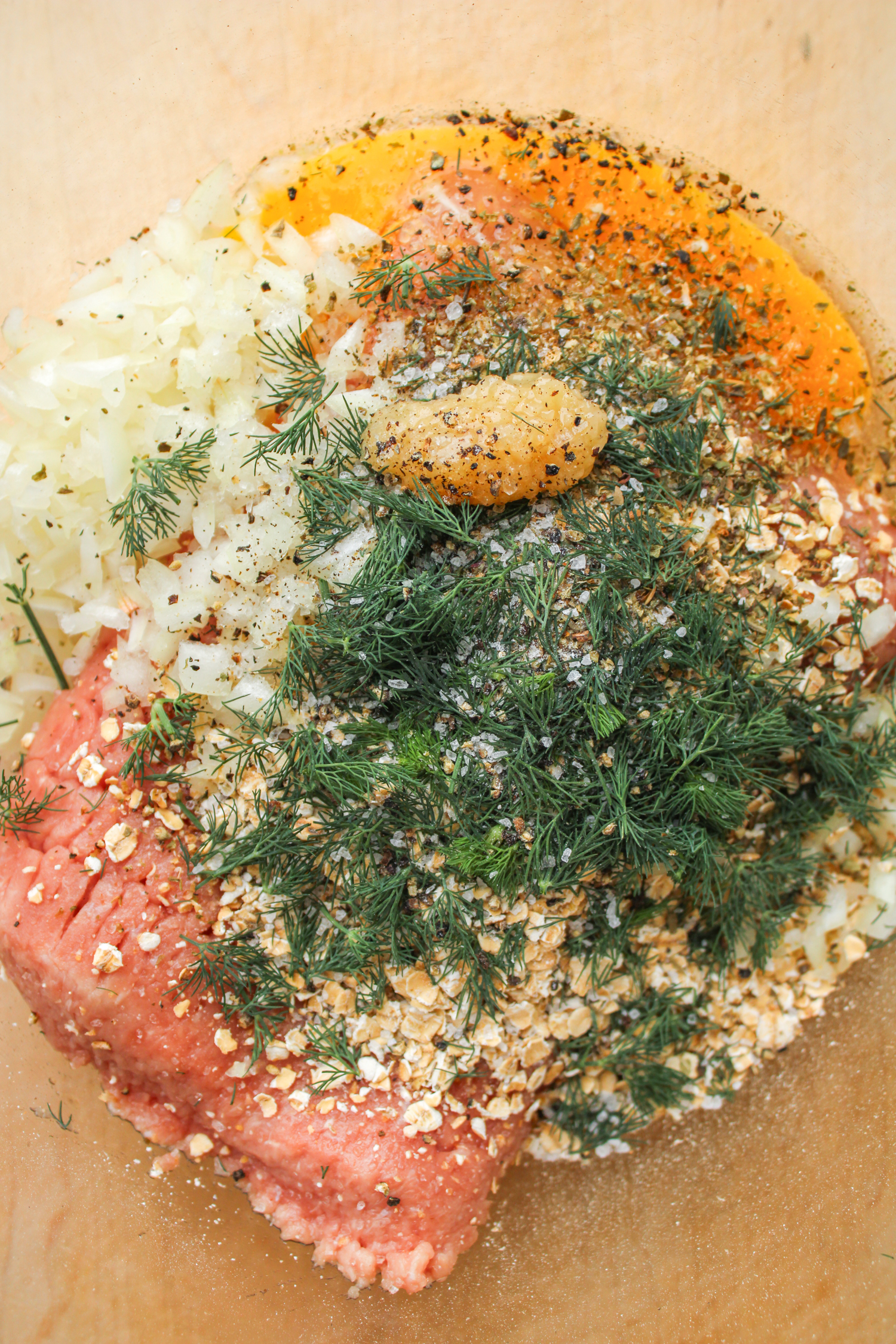 greek turkey burger ingredients in a glass bowl on top of a wooden cutting board