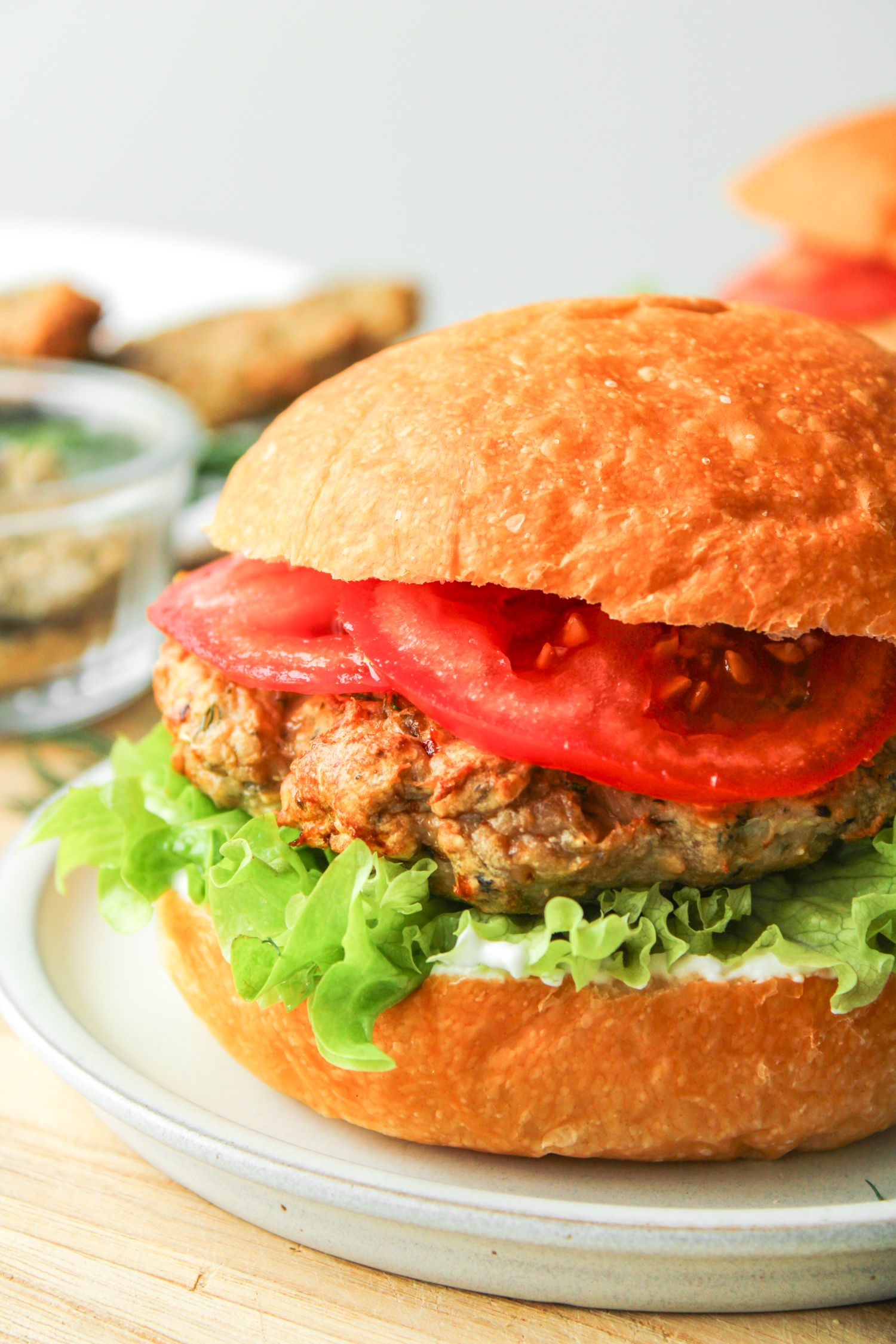 close up shot of air fryer turkey burger with lettuce, tomato and tzatziki in a hamburger bun on a grey ceramic plate 